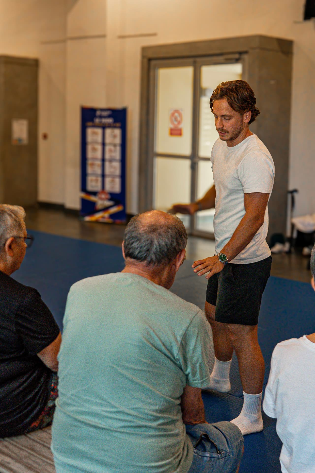Alix animant une séance de sport adaptée en groupe, seniors assis sur des tapis